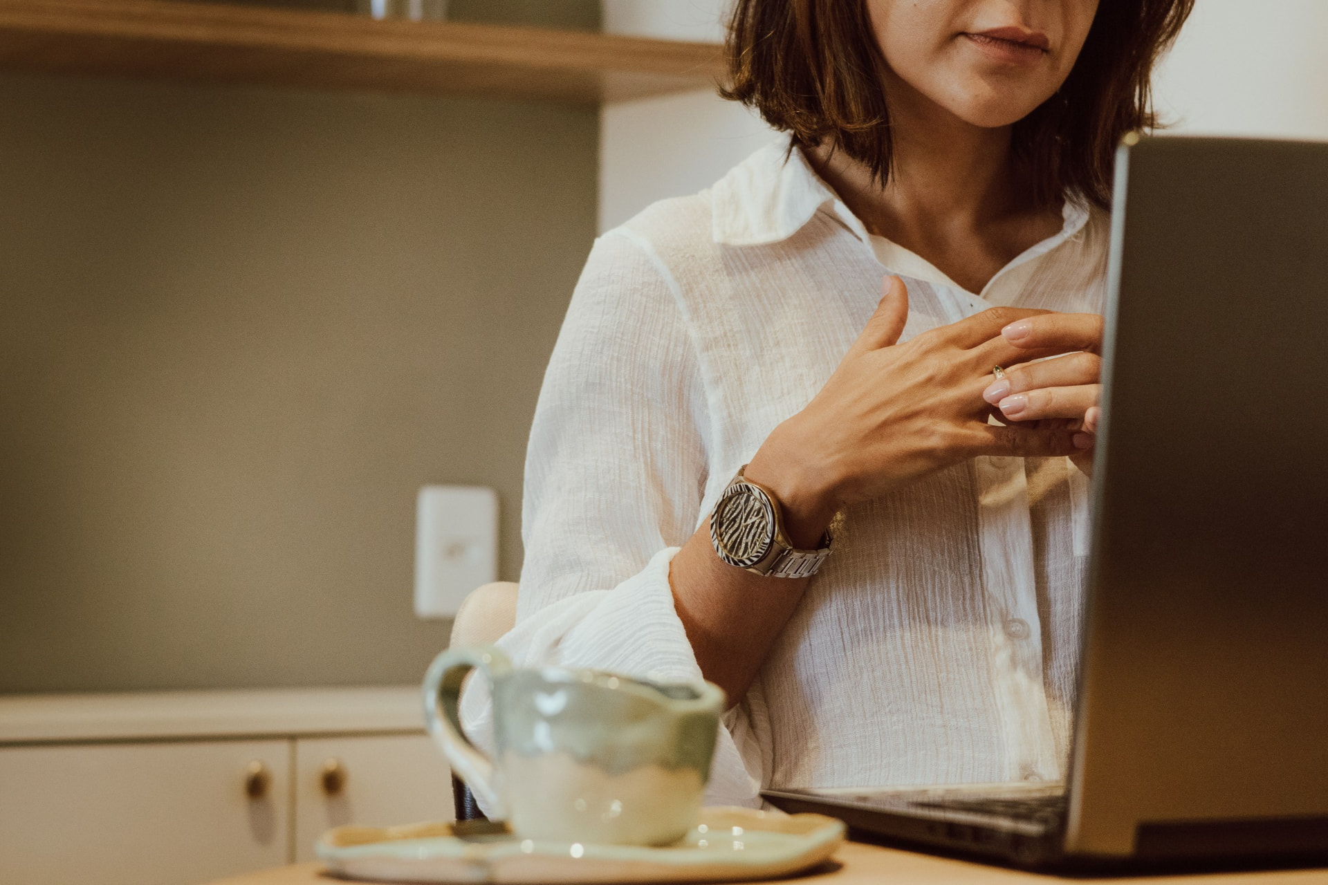 Débora Vieira Carpes trabalhando ao computador em seu consultório, com uma xícara de café sobre a mesa
