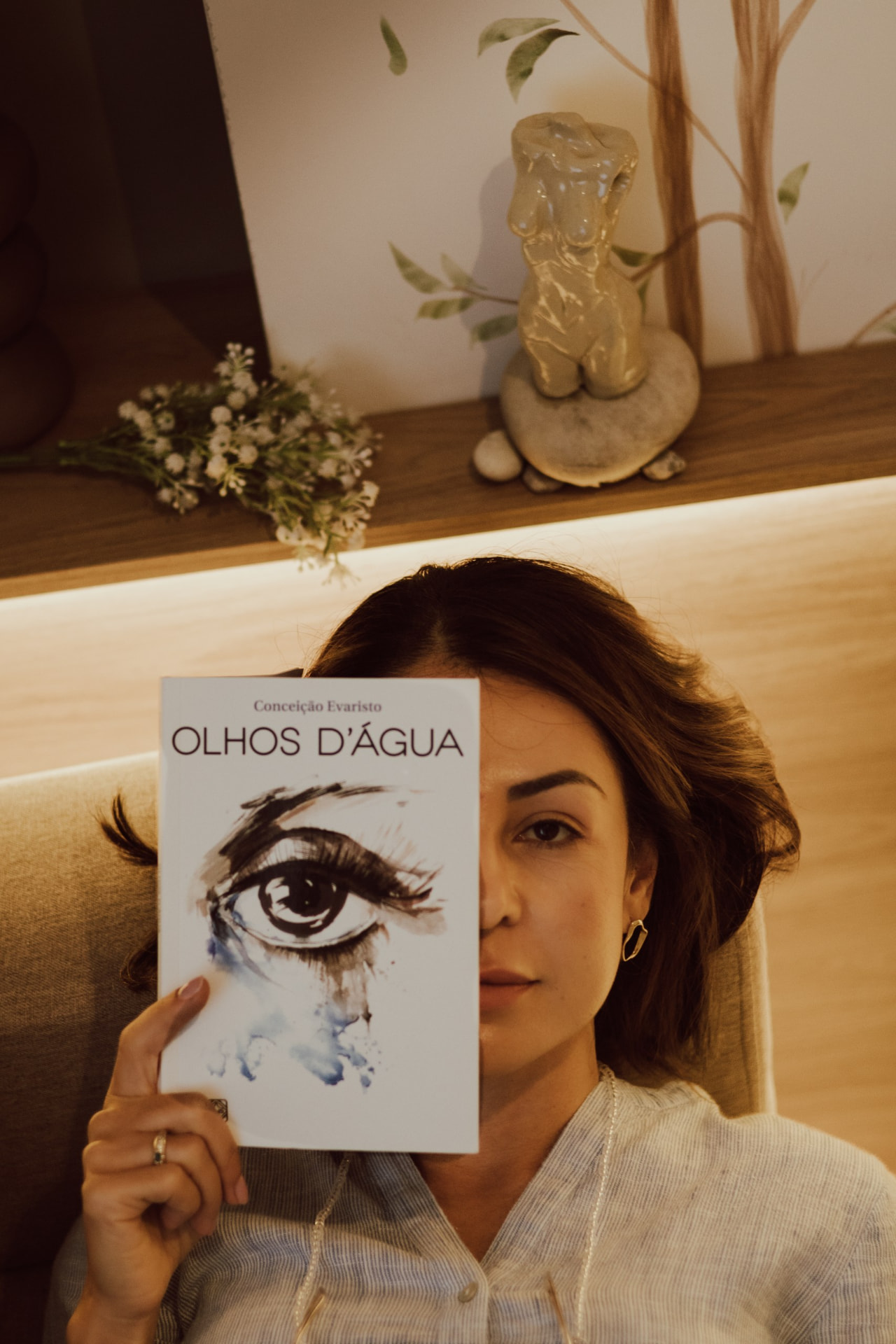Débora Vieira Carpes segurando o livro Olhos D'água, de Conceição Evaristo, parcialmente diante do rosto