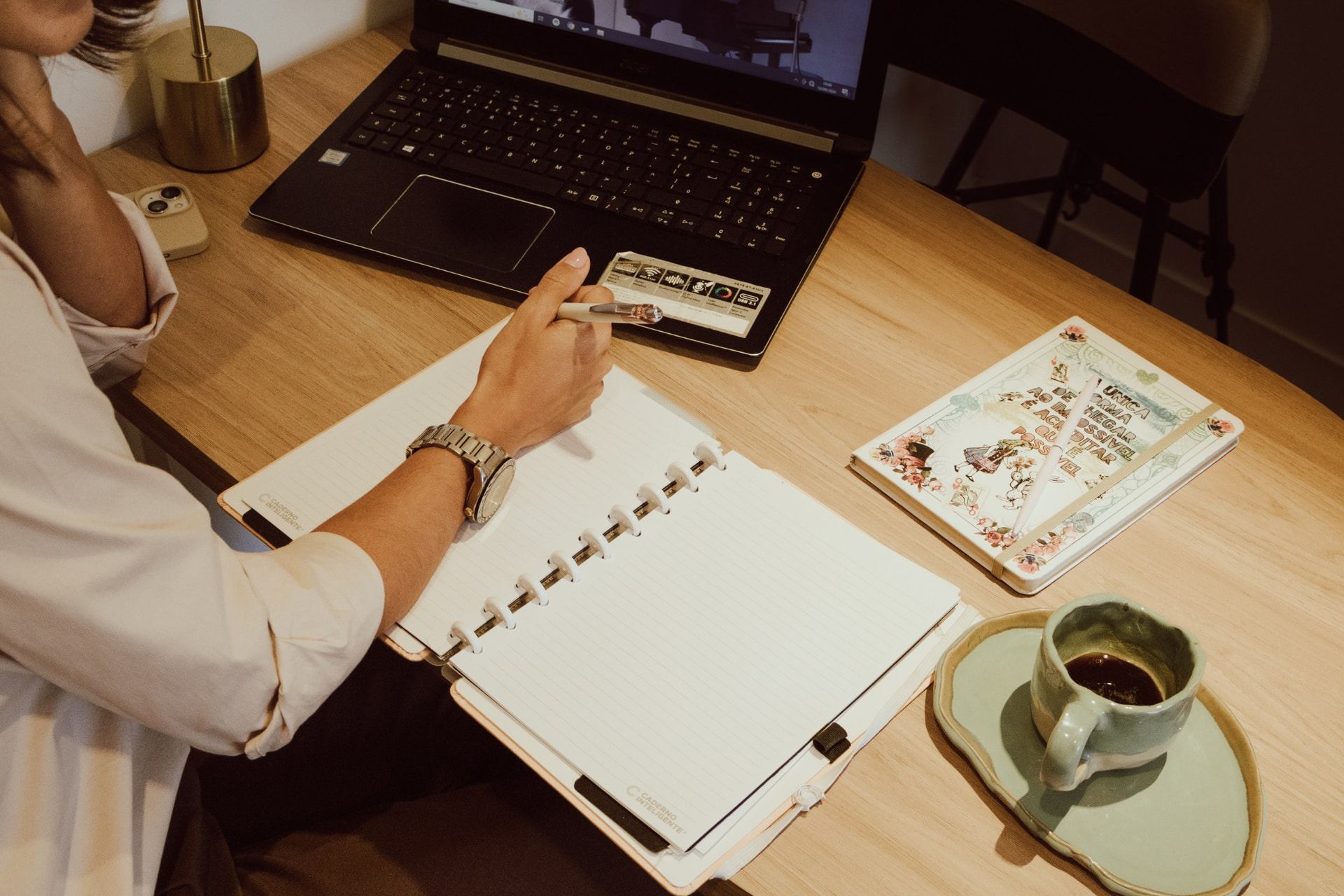 Mesa de trabalho com caderno, caneta, notebook e café