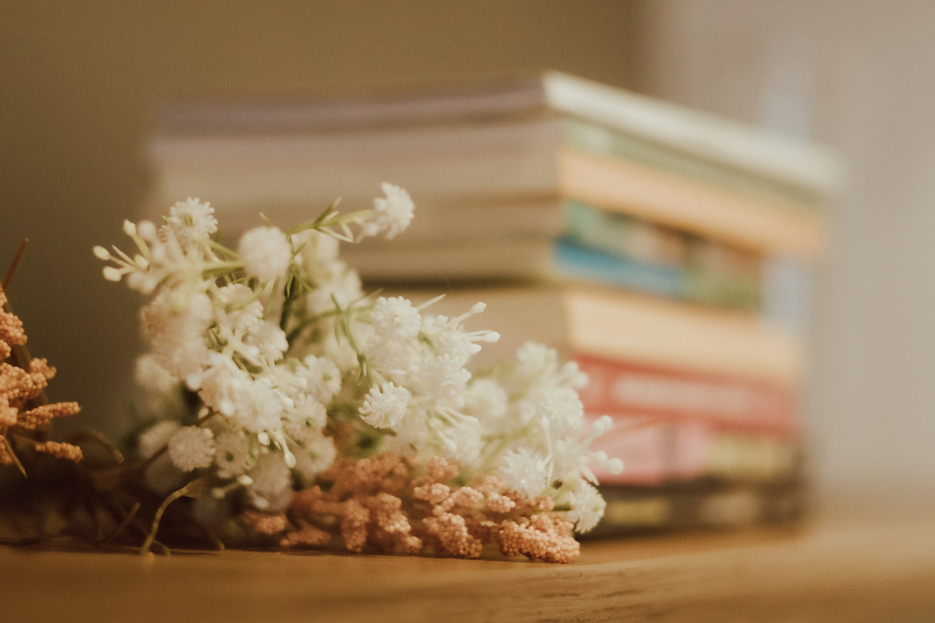 Flores brancas e ramos secos sobre mesa de madeira, com livros empilhados ao fundo